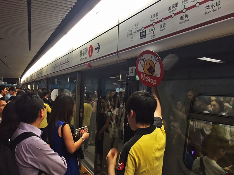 Hong Kong - As portas da plataforma do metrô tem um agente sinalizando com placa. Siga ou Pare!